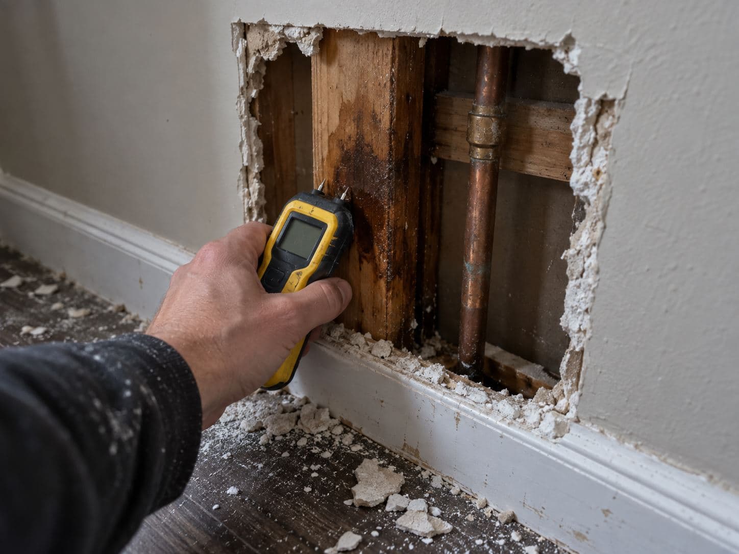 Inspection opening cut in drywall exposing a wet stud bay and copper supply line