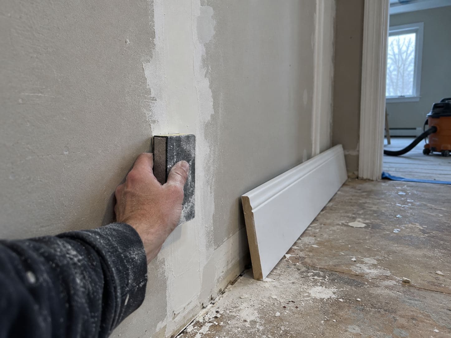 Taped and sanded drywall seam beside a run of newly fitted baseboard awaiting paint